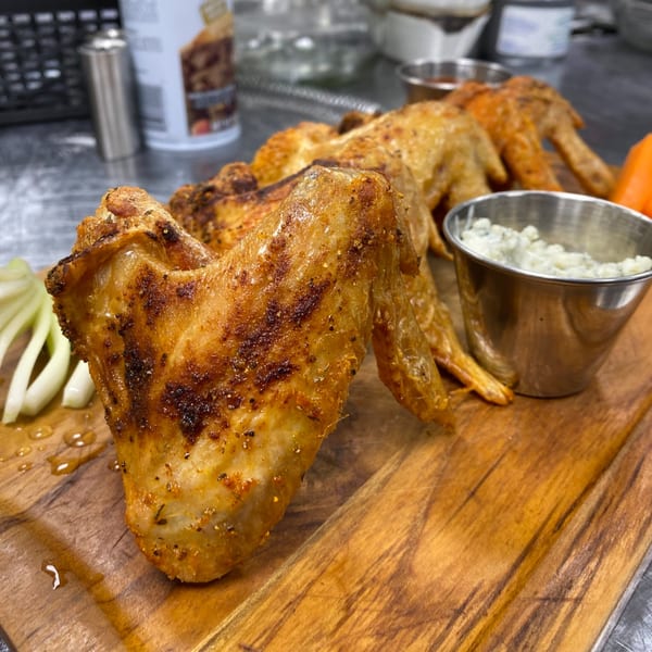Crispy chicken wings with dipping sauce and sliced onions on a wooden board at Rodney's at 436 Main.