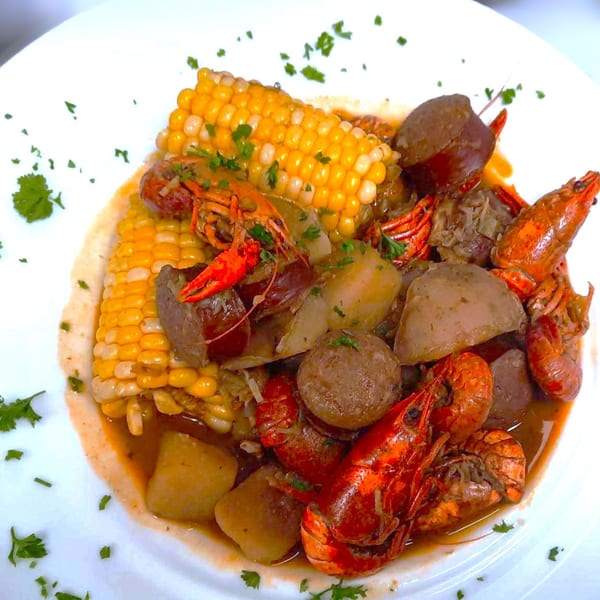A close-up of a seafood boil with crawfish, corn on the cob, potatoes, and sausage in broth.