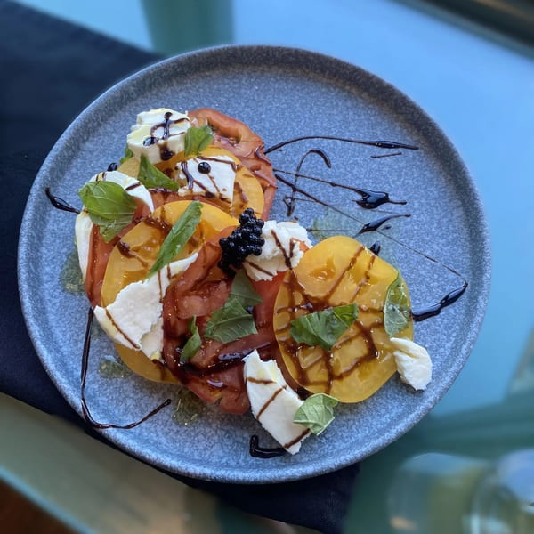 Heirloom tomato and mozzarella salad with basil, balsamic glaze, and caviar on a gray plate.
