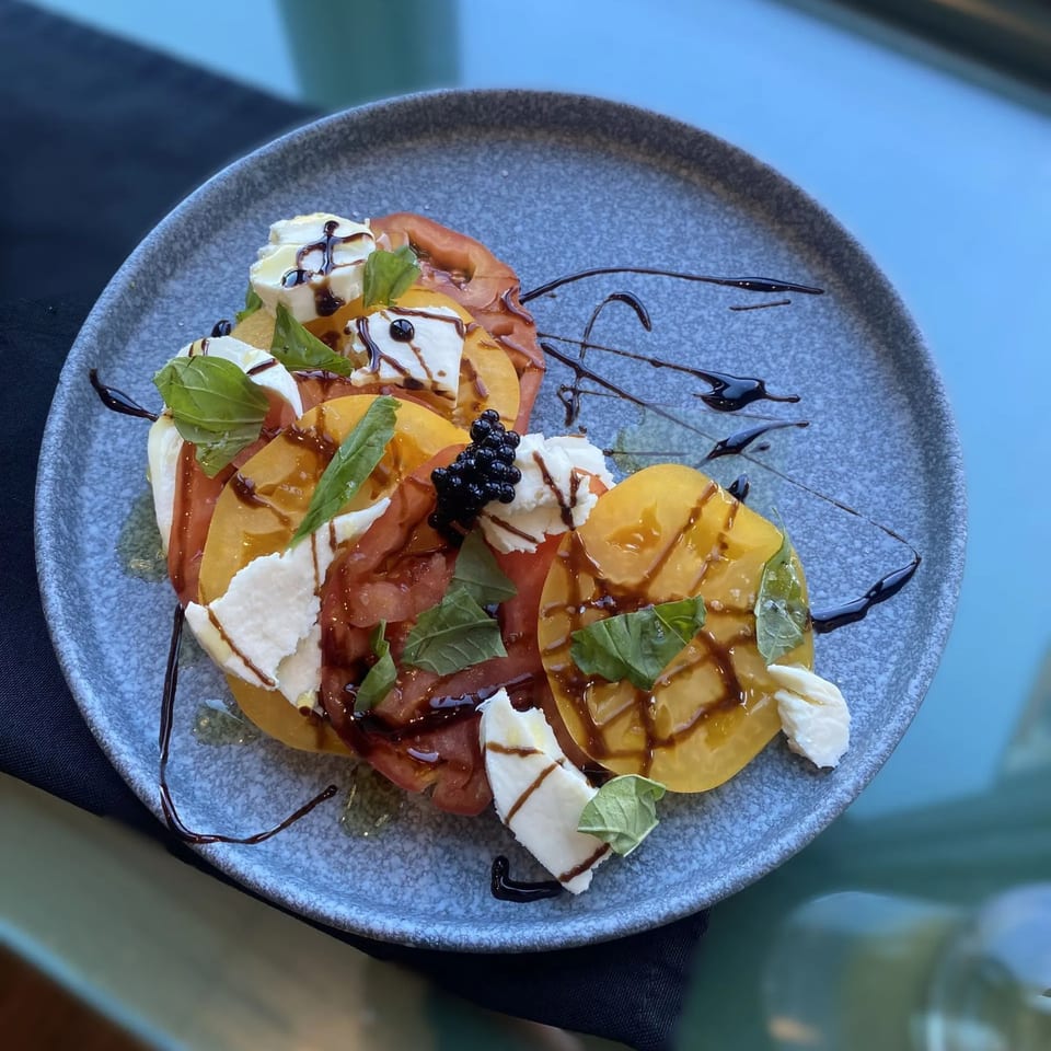 Heirloom tomato and mozzarella salad with basil, balsamic glaze, and caviar on a gray plate.
