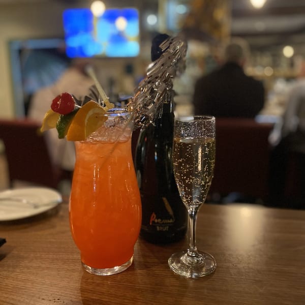 A vibrant orange cocktail with fruit garnish, a champagne flute, and a bottle on a wooden table.